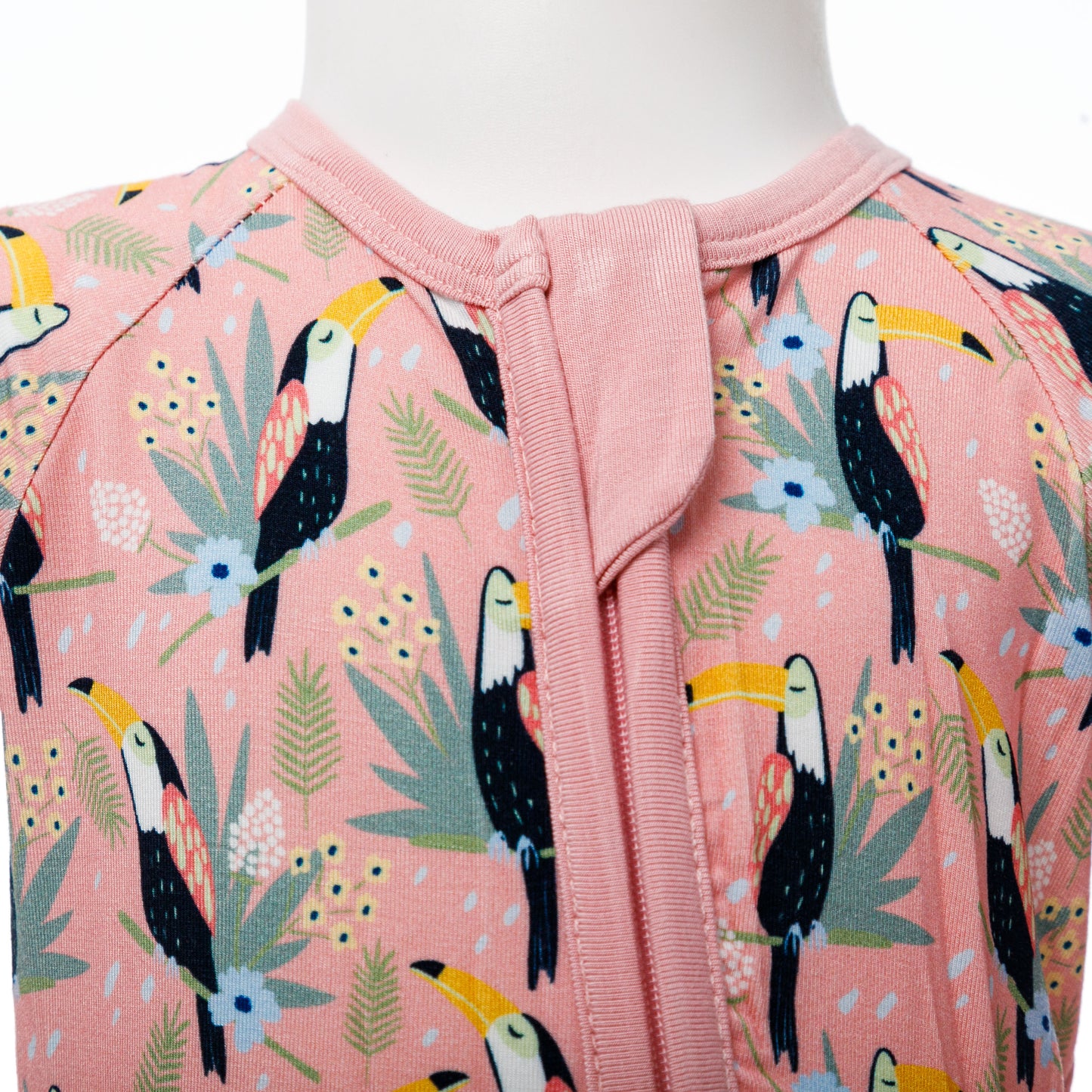 Vedere de aproape a fermoarului roz pe body-ul pentru bebeluși cu imprimeu de tucani.