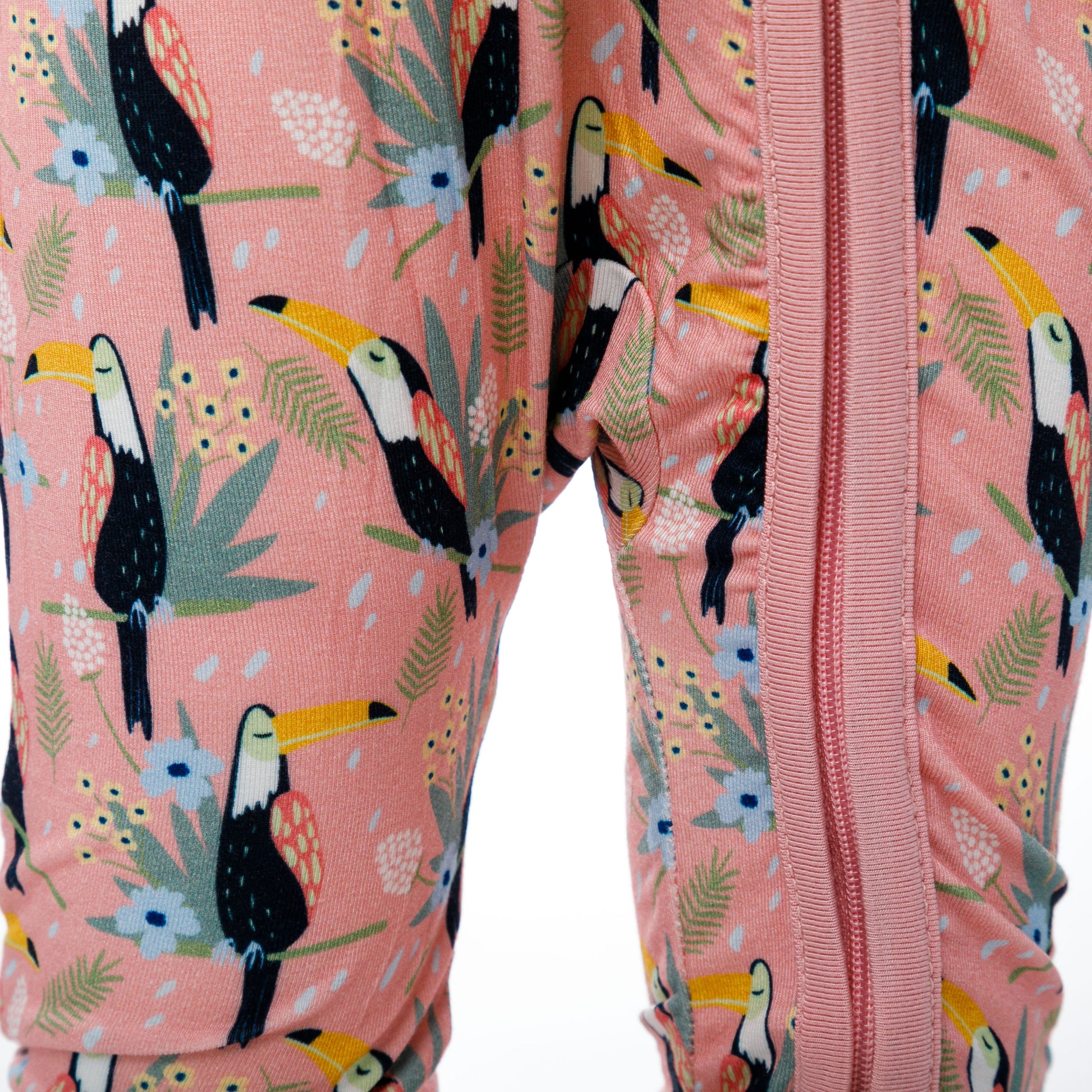 Vedere de aproape a fermoarului roz pe body-ul pentru bebeluși cu imprimeu de tucani.